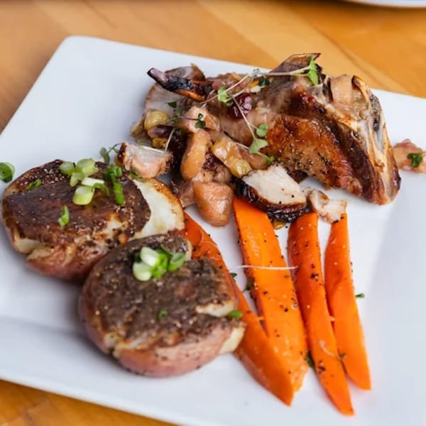 Fandee's Restaurant's grilled pork chop with smashed potatoes, carrots, and microgreens on a white plate.
