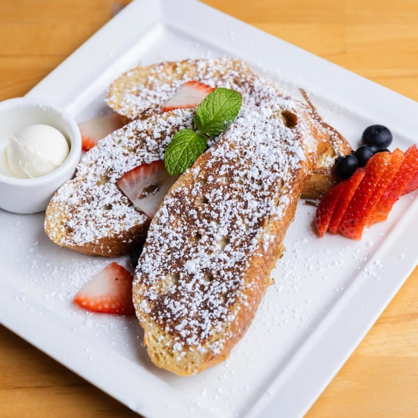 Fandee's French toast, powdered sugar, strawberries, blueberries, mint, and whipped cream on a white plate.