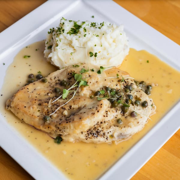 Fandee's chicken piccata with capers and mashed potatoes, drizzled with sauce on a white plate.