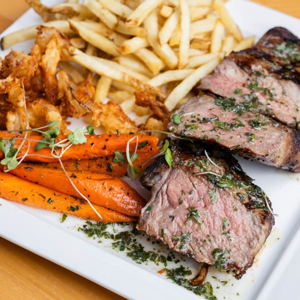 Fandee's Restaurant's steak with fries, roasted carrots, and crispy fried onions on a white plate.