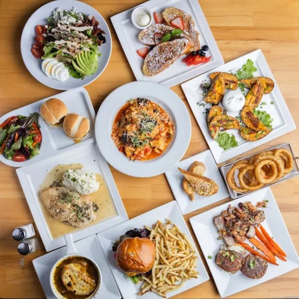 An overhead view of a wooden table laden with various diner dishes, including pasta, salads, and burgers.