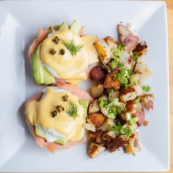 Two Fandee's Restaurant Eggs Benedict with salmon, avocado, capers, and dill, served with breakfast potatoes.