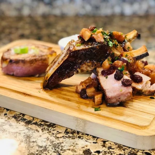 Fandee's Restaurant pork chop with apples, cranberries, and a side of potato on a wooden board.